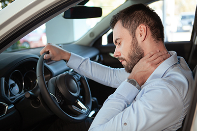 Young man rubbing his aching neck, looking tired from driving. Male driver having neck pain, sitting in his car