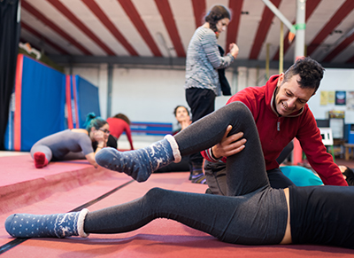 Coach helping woman to stretch leg muscles lying on mat in gymnasium.